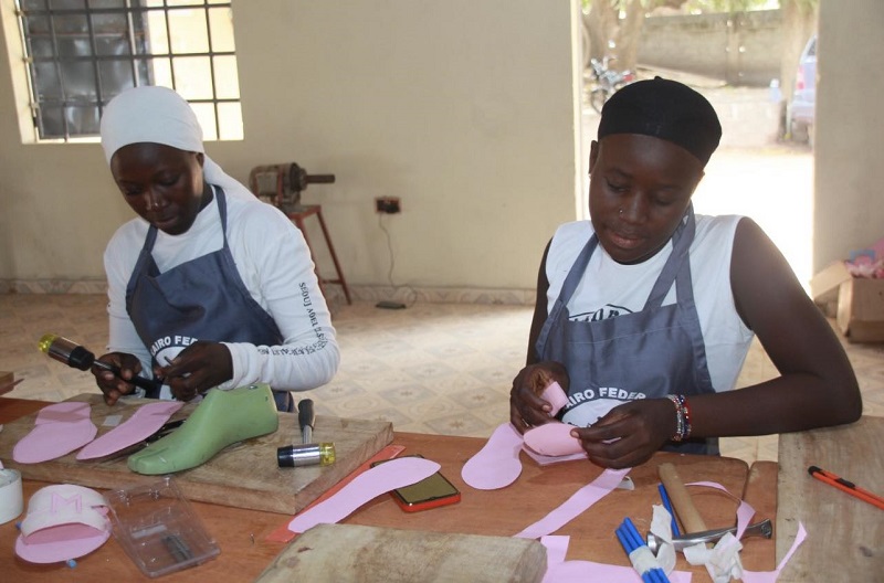 Teen girls sit at a table making shoes in The Gambia