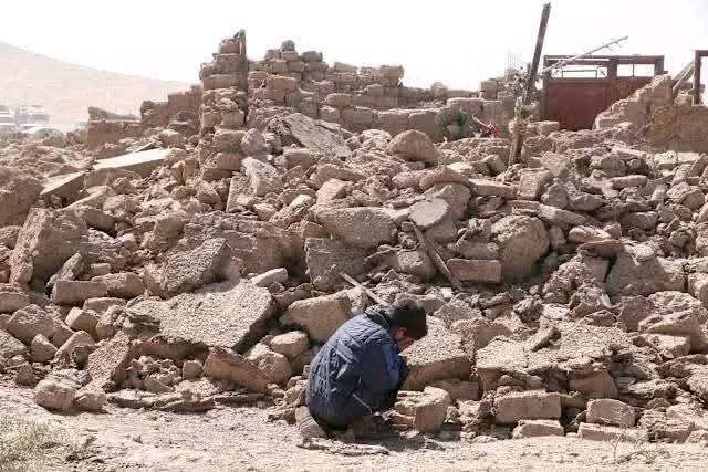 A boy bends down to cry in front of rubble after the Afghanistan earthquake.