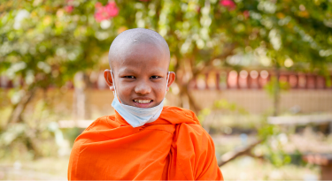 Smiling young Buddhist novice monk in an orange robe, symbolizing peace and learning.